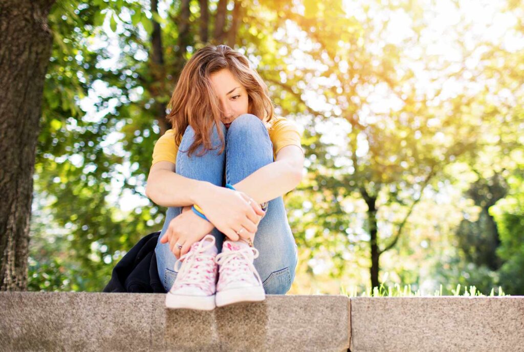 Sad woman sitting on a wall in a park